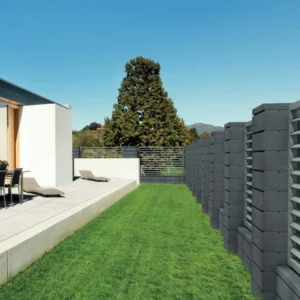 Ogrodzenie Semmelrock LORDIO w kolorze antracyt (grafit) – murek z filarami i daszkami wzdłuż trawnika przy tarasie.